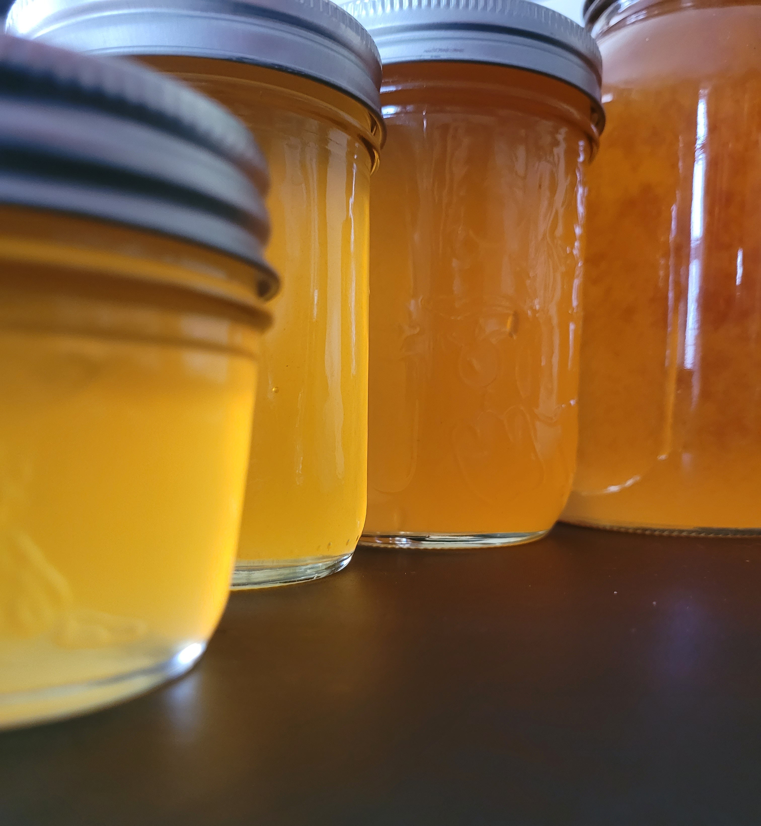 Close-up of multiple size jars. The product in the jars is Apple Juice Jelly, on a black surface.
